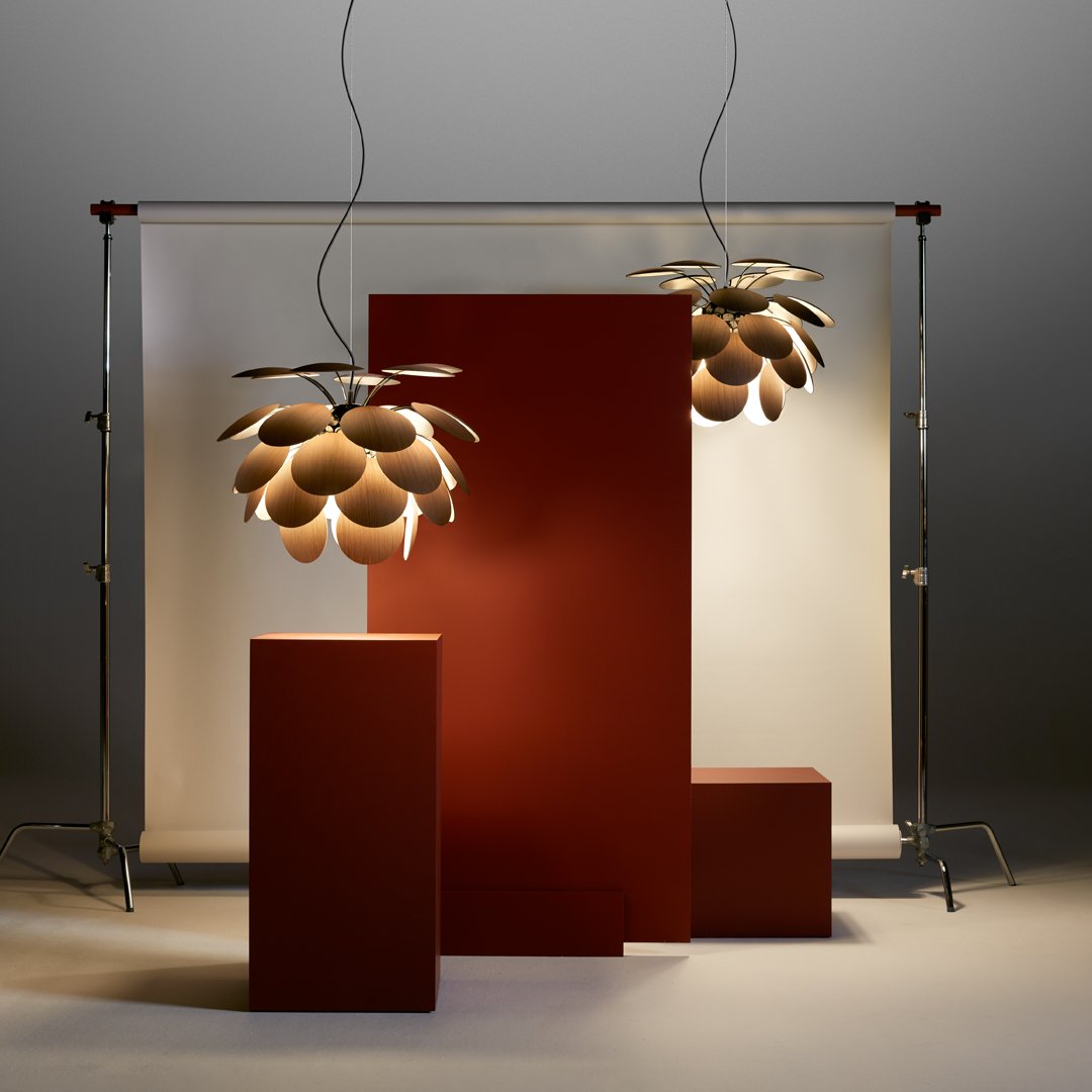 Modern pendant lights with gold and brown tones, displayed against red geometric structures on a neutral backdrop.
