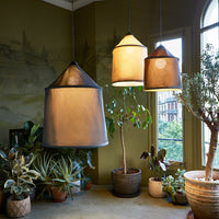 "Three modern hanging lamps in warm tones of amber and beige with sleek black accents, surrounded by lush greenery."
