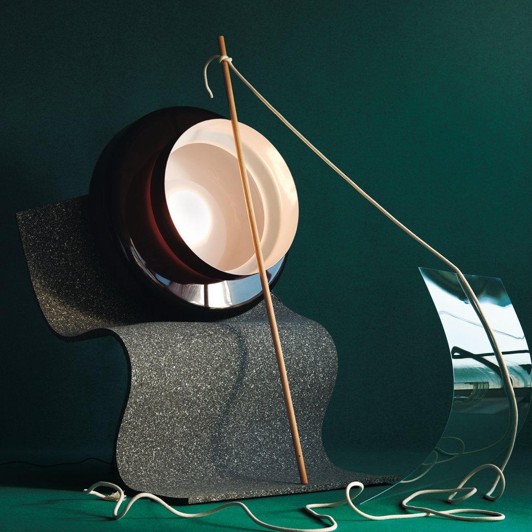 Contemporary lamp featuring a glossy black base, smooth beige dome, and sleek silver accents against a dark green backdrop.