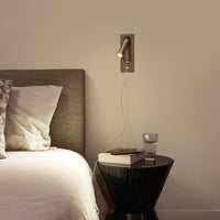 Modern wall lamp in brushed metal with a minimalist design; soft gray bedding and geometric pillow patterns.