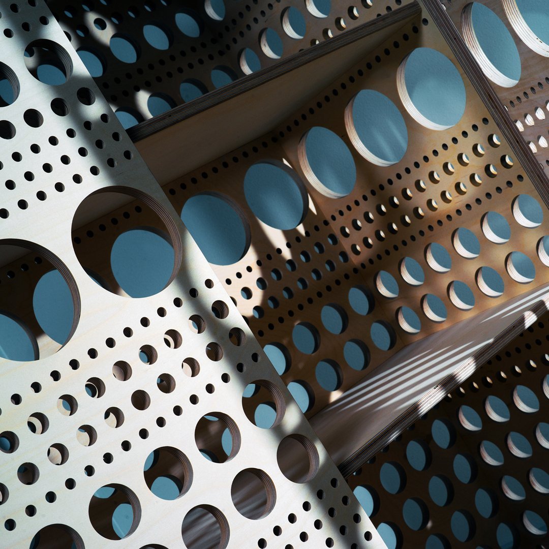 Light wooden board with alternating patterns of circular and dotted holes in varying sizes. Blue background enhances depth.
