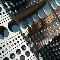 Light wooden board with alternating patterns of circular and dotted holes in varying sizes. Blue background enhances depth.