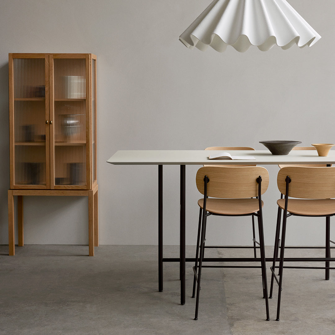Minimalist wooden furniture with natural tones, light beige table, structured dark legs, and soft white lamp shade.