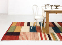 Multicolored geometric patterned rug featuring reds, greens, yellows, and creams, placed under a wooden table.