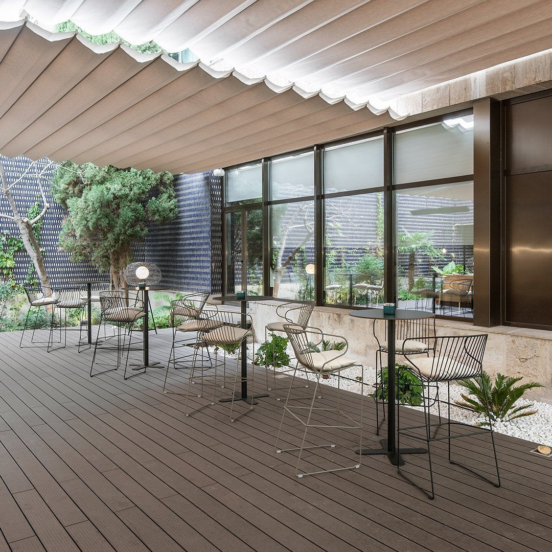 Stylish outdoor seating area featuring neutral tones, textured wood flooring, and sleek metal chairs against a green backdrop.
