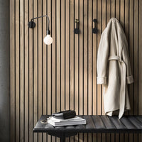 Cozy cream robe against vertical wooden slats, accented by a black lamp and dark table, creating a warm, modern look.