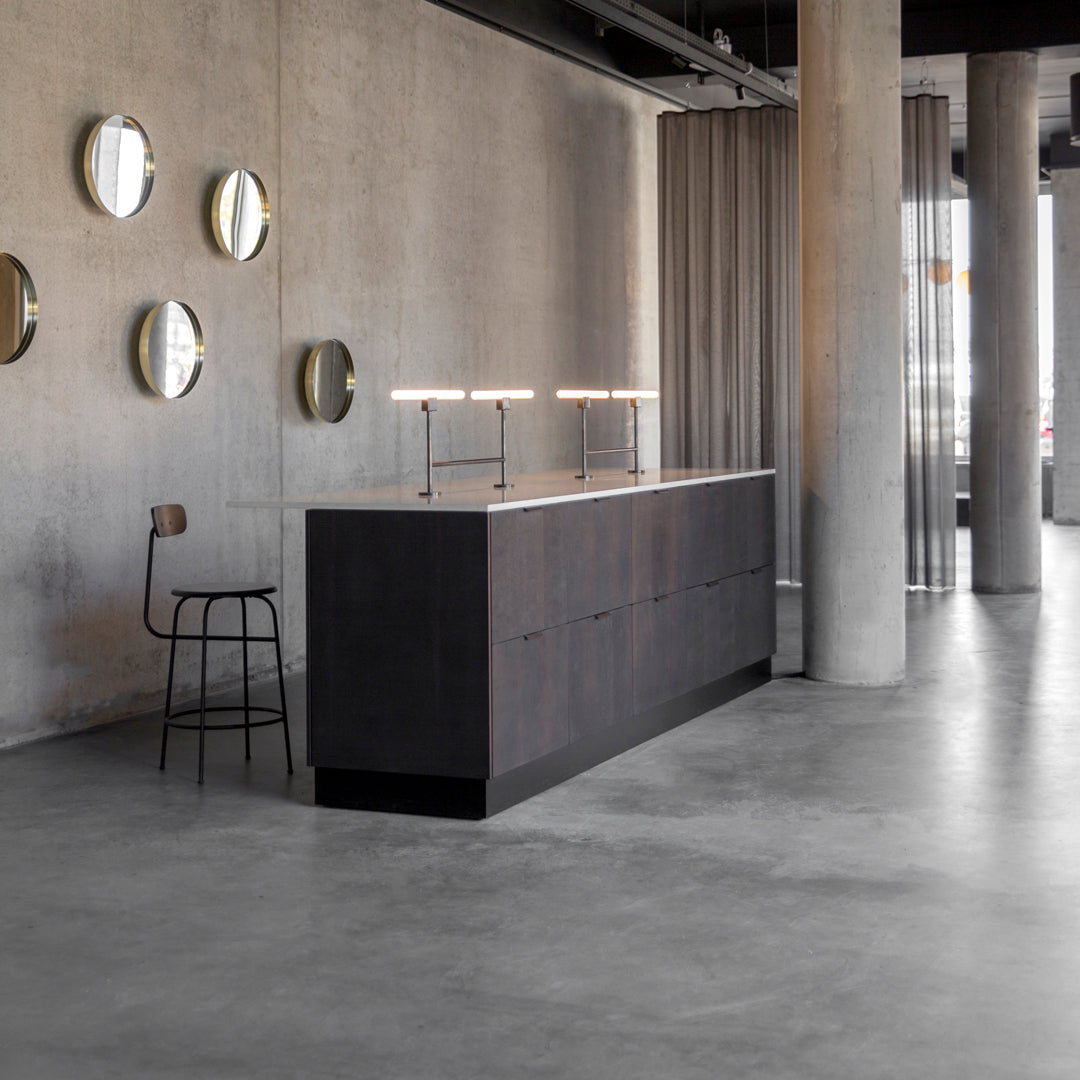 "Sleek black cabinetry with a minimalist finish, paired with round silver mirrors and a gray concrete floor."