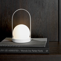 White dome lamp with a circular base and handle, placed on a dark wood surface, contrasting with patterned book covers.
