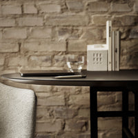 Stylish gray chair beside a round black table, set against a textured beige brick wall for a modern look.