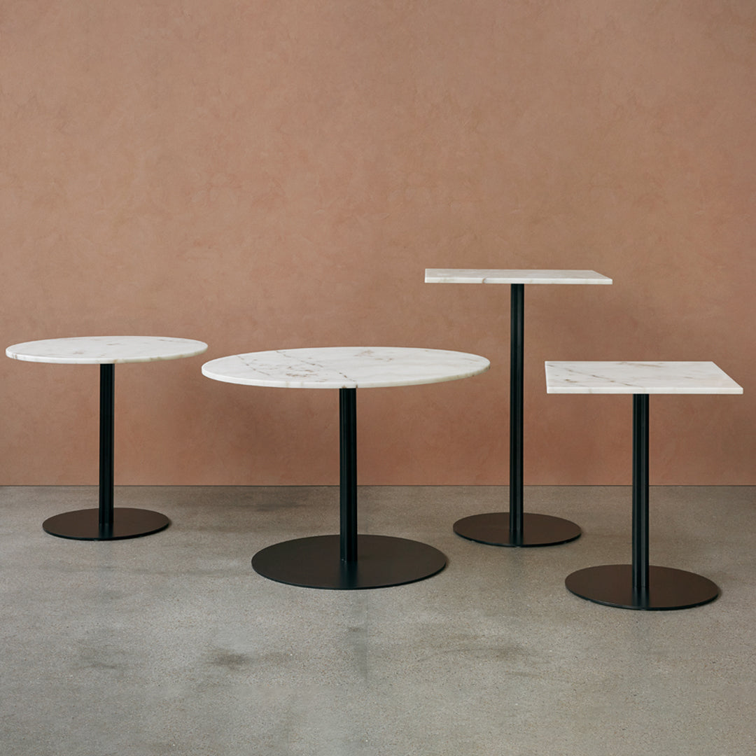 Set of four tables featuring white marble tops with black bases, showcasing modern minimalism against a warm backdrop.