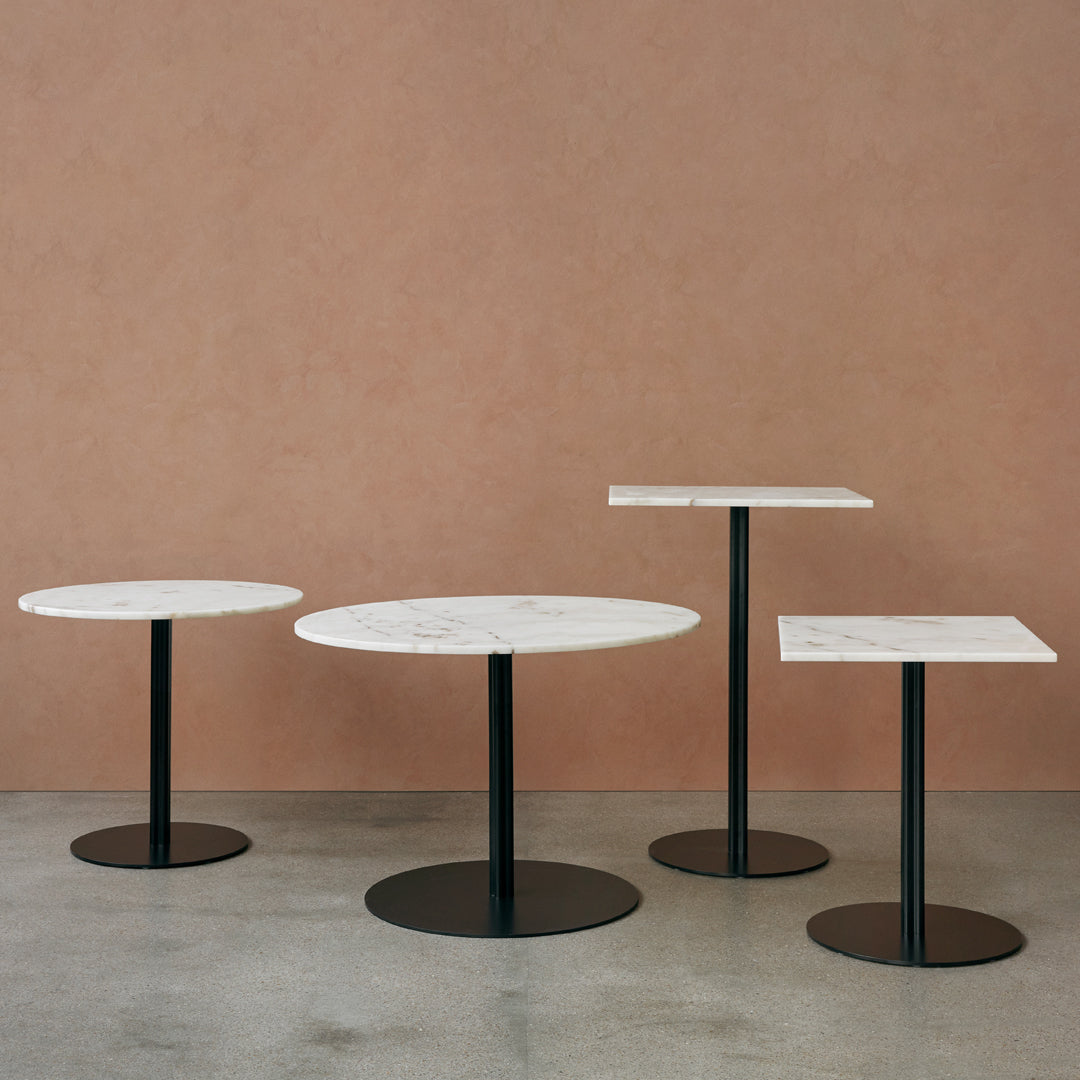 Set of three modern tables with white marble tops and sleek black bases against a warm pastel background.