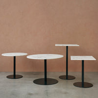 Set of three modern tables with white marble tops and sleek black bases against a warm pastel background.