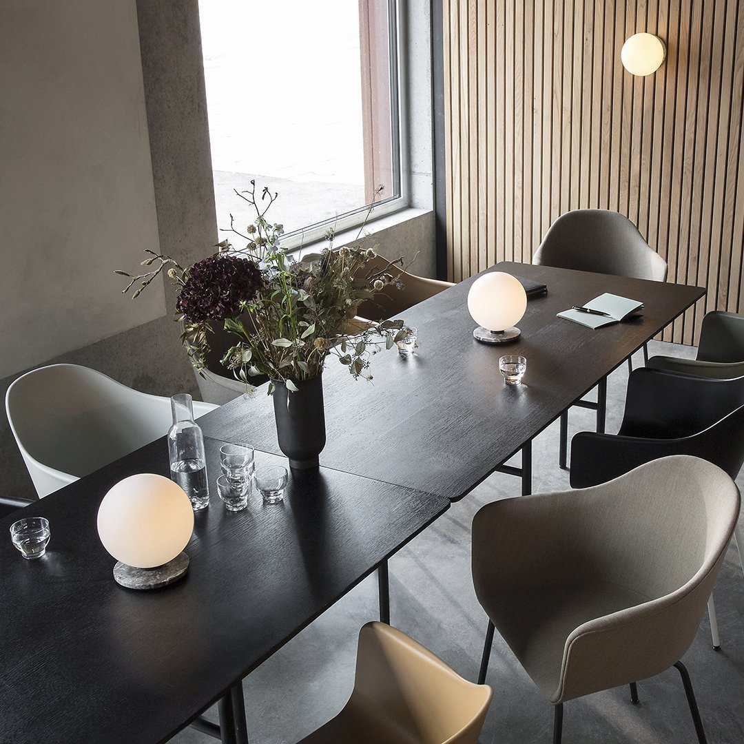 Modern dining area featuring a black table, muted gray and beige chairs, and a soft white round lamp with a natural wood backdrop.