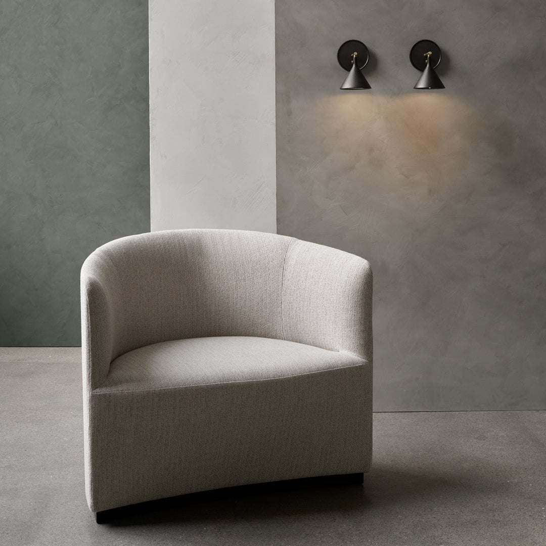 Curved beige armchair against a muted gray wall, featuring soft textures and minimalist design.