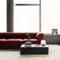 Deep red sofa with soft fabric, paired with a sleek black coffee table on a neutral-colored rug. Modern, minimalist design.