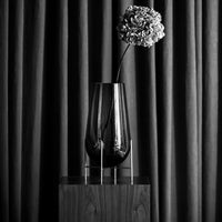 Black glass vase with a modern design, featuring a delicate flower against textured dark gray curtains.