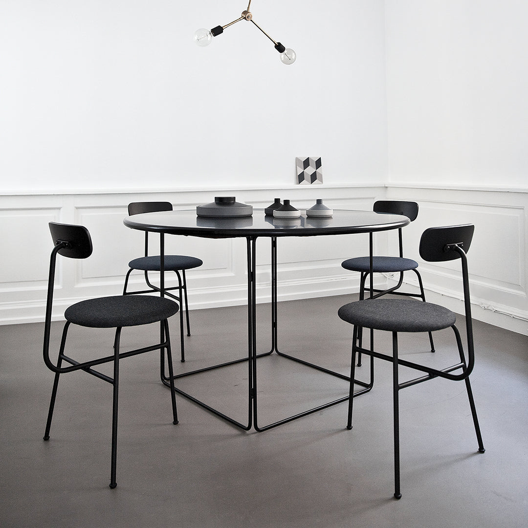Modern black dining table and chairs with gray upholstery against a minimalist white backdrop. Geometric decor accents in gray.