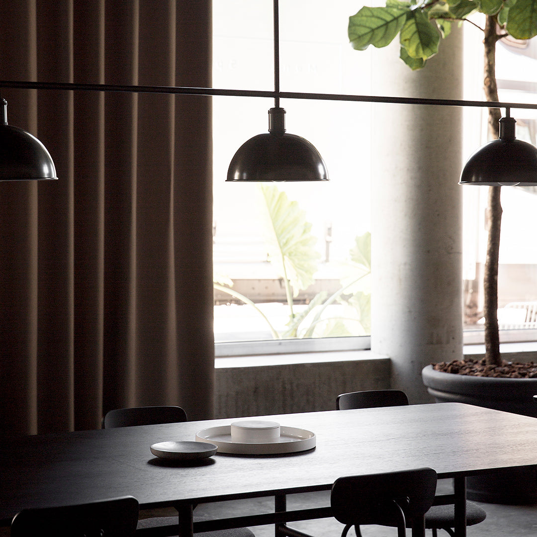 Black pendant lights, beige curtains, dark wood table, white ceramic dishes, and green plant accents.