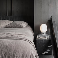 Soft gray bedding set layered over a textured black nightstand, highlighted by a white lamp for contrast.