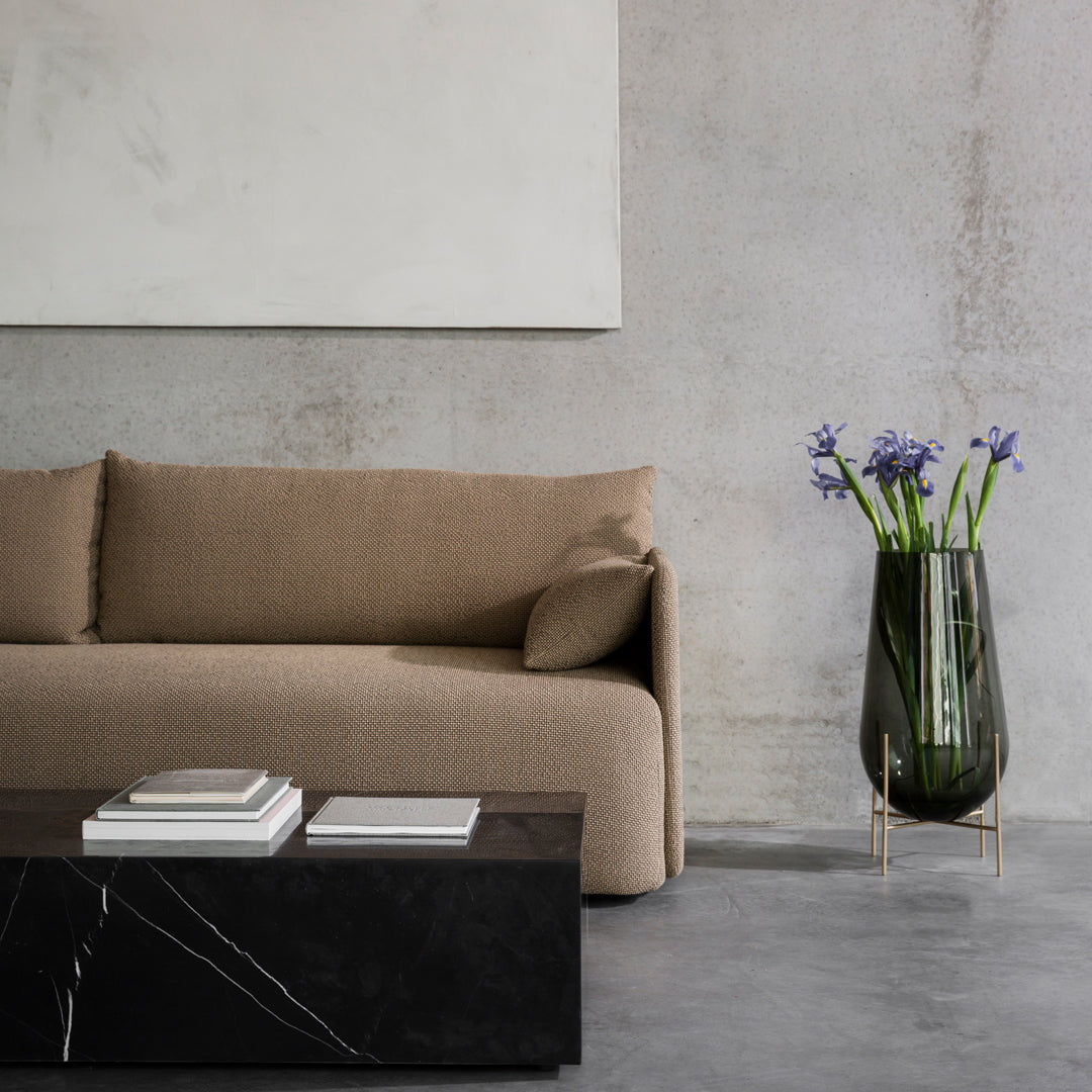 Beige textured sofa paired with a sleek black geometric coffee table and a stylish green glass vase with purple flowers.