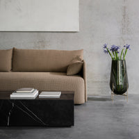 Modern beige quilted sofa with a sleek black marble coffee table and a dark glass vase featuring blue flowers.
