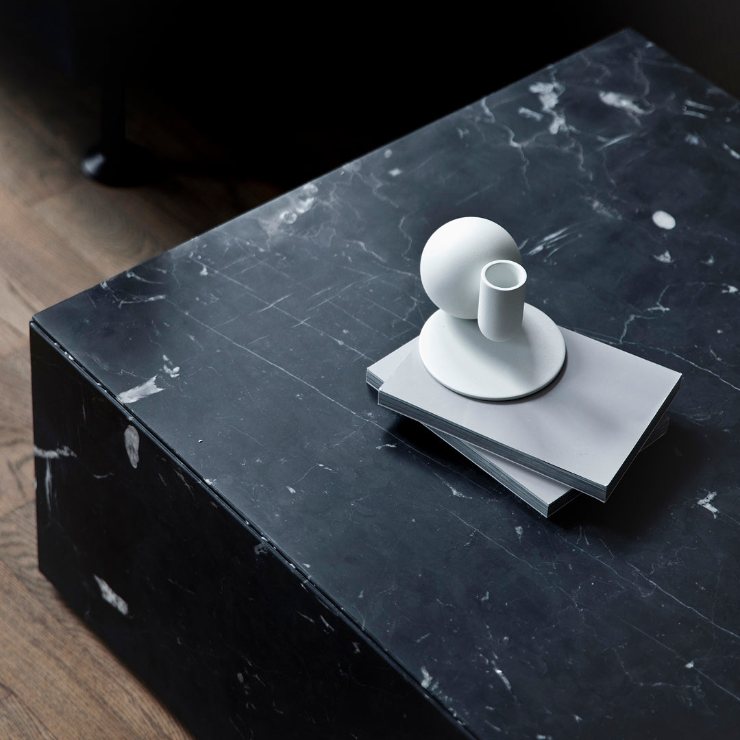 White ceramic candle holder on a grey tray, displayed on a sleek black marble surface with subtle veining.