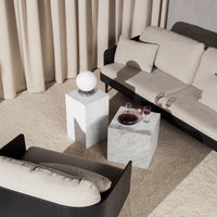 Modern living room with beige tones, white marble tables, and a sleek black couch against soft, neutral curtains.
