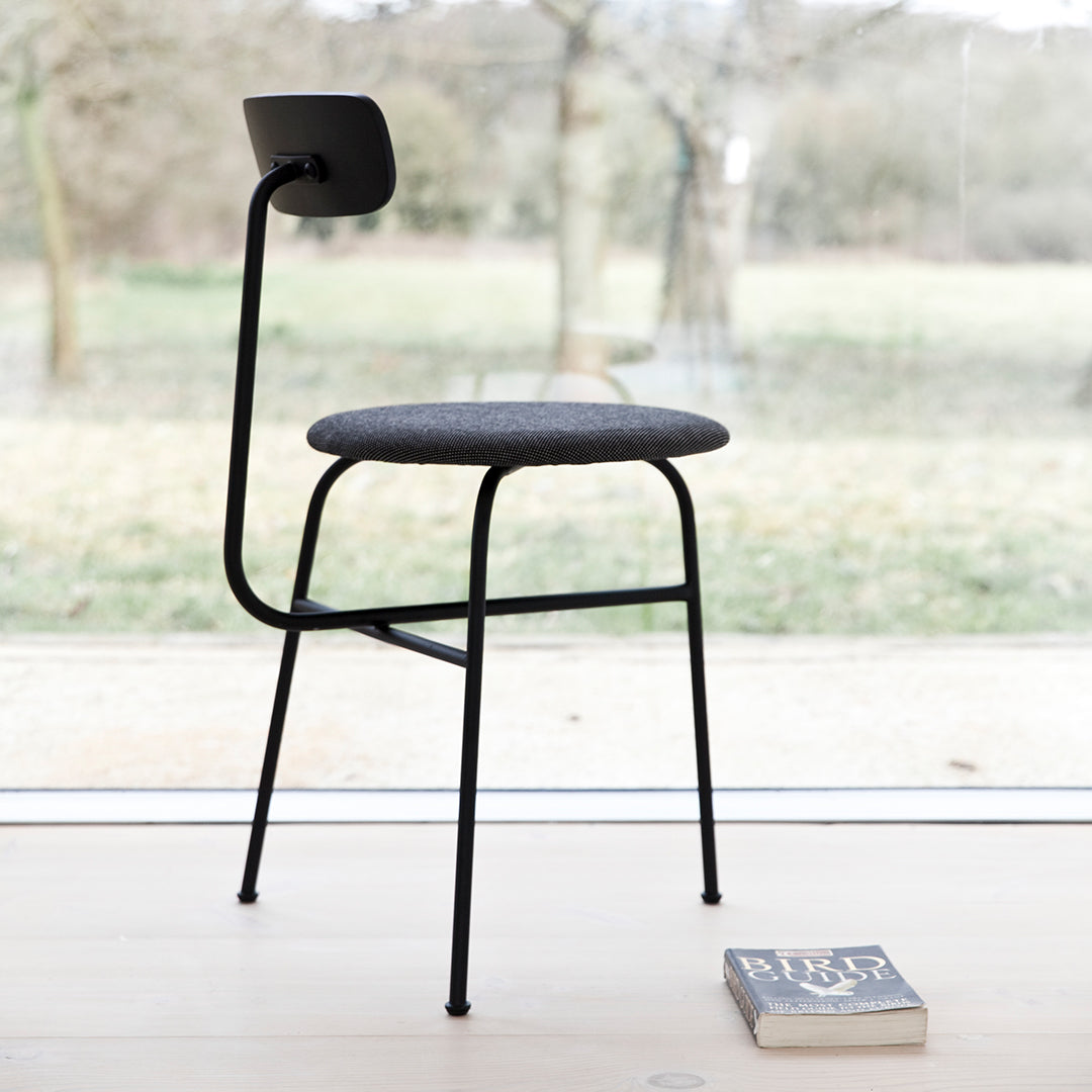 Black metal chair with a textured dark gray seat, set against a natural, light background. Minimalist design.