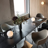Stylish table setup featuring black wood, neutral-toned chairs, and soft white lamp accents amidst floral arrangement.