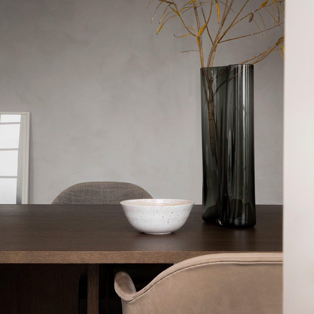 Modern dining scene featuring a textured black glass vase, minimalist white bowl, and neutral wood tones.