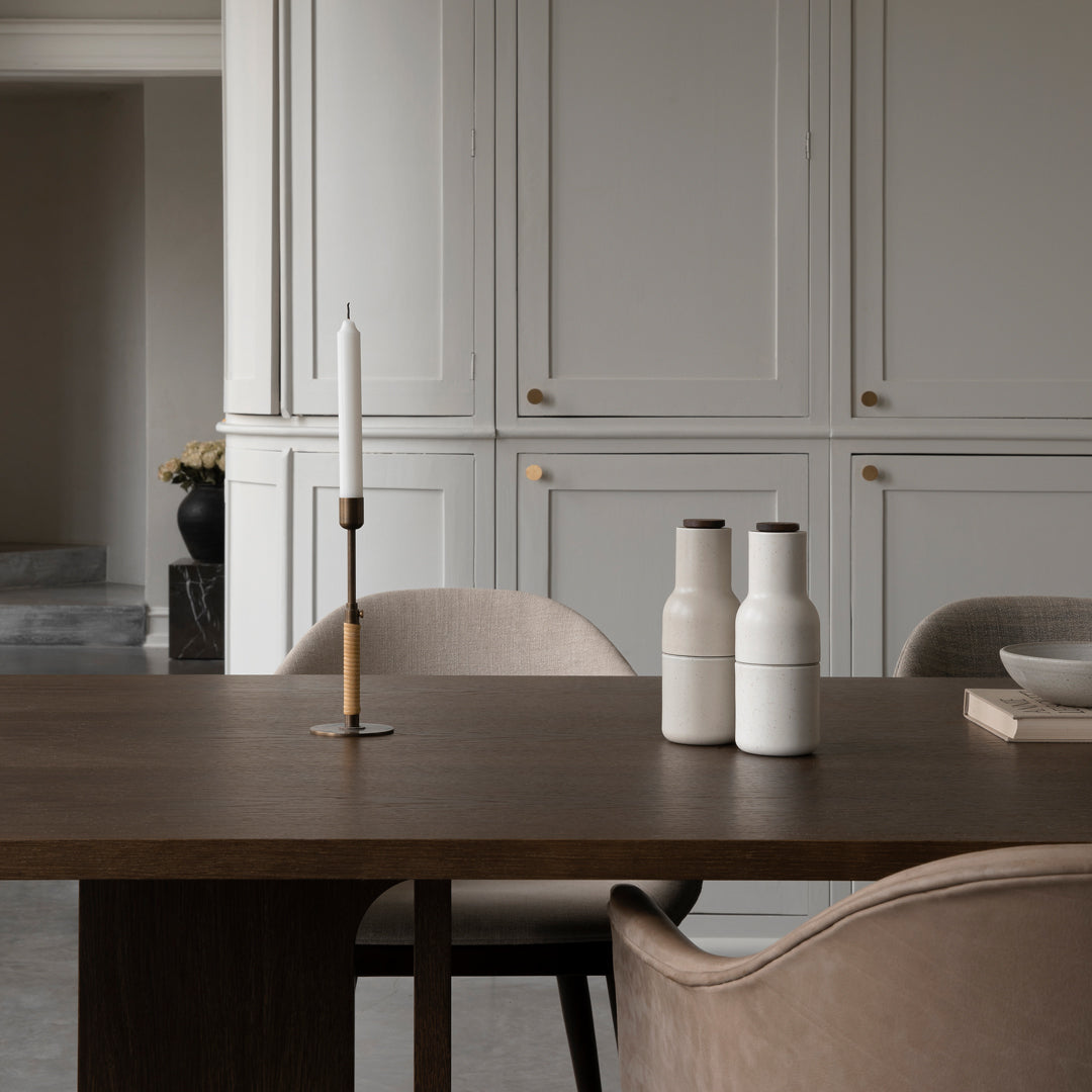 Minimalist white vases with dark accents on a warm wooden table, featuring soft beige chairs and neutral decor.
