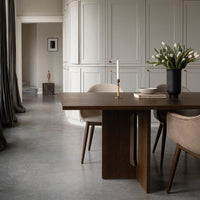 Elegant wooden table with soft beige chairs, set against a muted gray floor and warm, neutral wall tones.