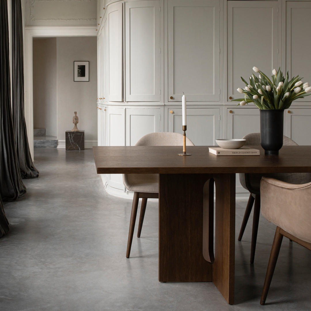 Elegant brown wood dining table with beige chairs against a softly textured gray floor and neutral-toned walls.