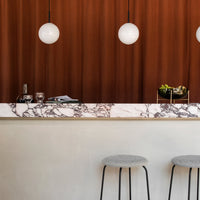 Brown backdrop with marble-patterned countertop and gray stools, accented by white pendant lights.