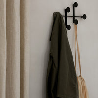 Olive green jacket and beige curtain hanging on a minimalist black wall hook against a neutral backdrop.