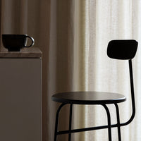 Minimalist black chair and cup against soft, neutral curtains, highlighting sleek lines and subtle textures.
