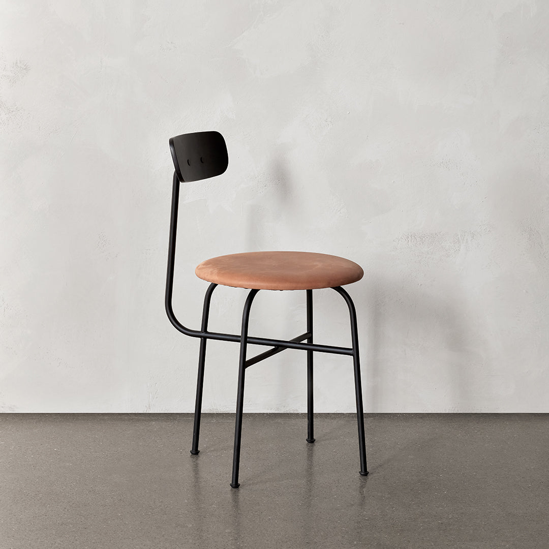 Black metal chair with a round, natural terracotta seat against a light gray background. Simple and modern design.