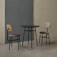 Stylish black round table with soft pink and wood-accented chairs against gray and beige walls. Modern minimalist design.