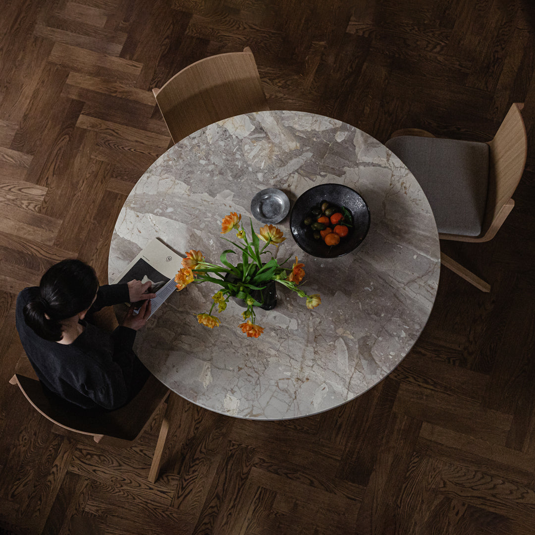 Round marble table with gray veining, complemented by a black bowl and vibrant floral arrangement on a wooden floor.