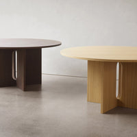 Two round tables, one in dark wood and the other in light yellow wood, featuring minimalistic, modern designs.