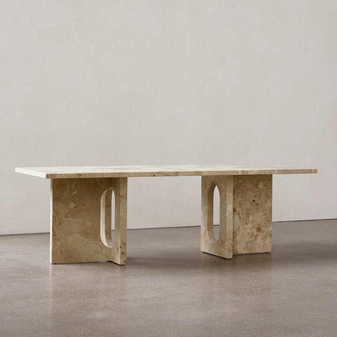 Neutral beige stone table with a smooth surface and geometric cut-out patterns on the sturdy legs. Minimalist design.