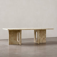 Neutral beige stone table with a smooth surface and geometric cut-out patterns on the sturdy legs. Minimalist design.