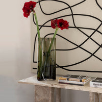 Transparent black vase with red flowers, against a backdrop of abstract black lines on a cream wall.