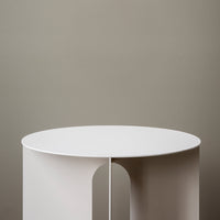 White circular table against a muted brown wall, featuring a sleek, modern design with smooth lines.