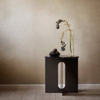 Black side table with a smooth, glossy top and a minimalist cut-out design against a warm, textured beige wall.