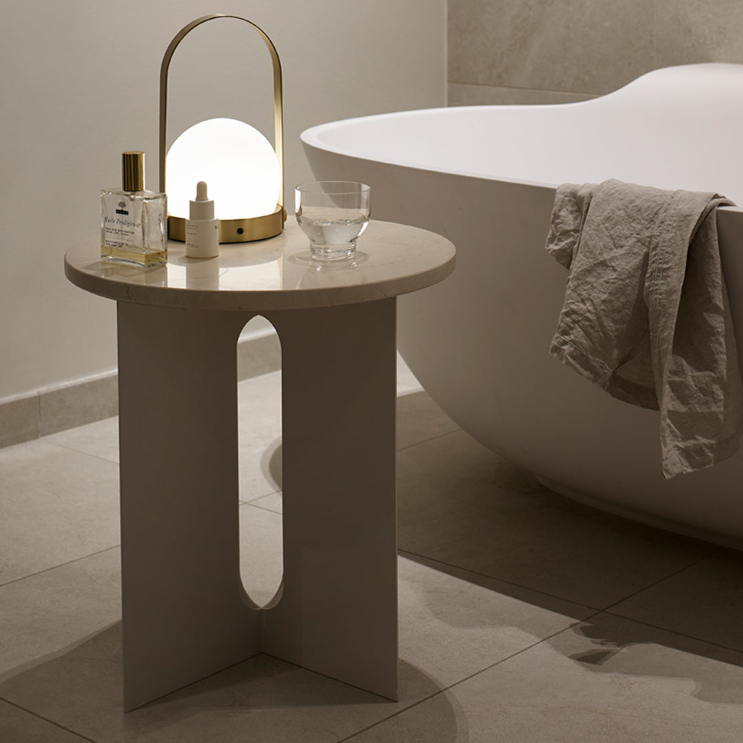 Modern gray side table with curved cutout design, paired with soft beige textures and warm lighting accents. Perfect for decor.