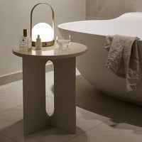 Modern gray side table with curved cutout design, paired with soft beige textures and warm lighting accents. Perfect for decor.