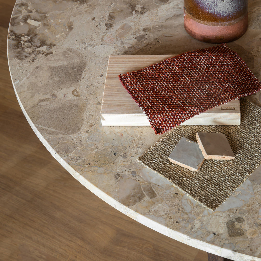 "Textured red woven fabric, beige wood blocks, and gray ceramic tiles on a round marble table with a natural finish."
