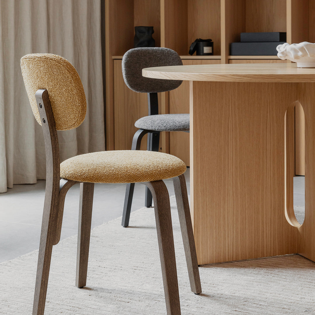 Two modern dining chairs in beige and gray fabrics with wooden legs, set against a warm wooden table and neutral decor.