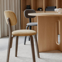 Two modern dining chairs in beige and gray fabrics with wooden legs, set against a warm wooden table and neutral decor.